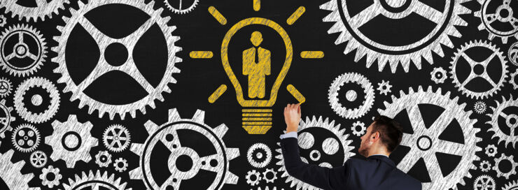 A man is drawing on a blackboard with gears and light bulb