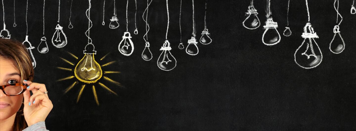 Young woman standing with her back against a blackboard where drawing shows multiple light bulbs.